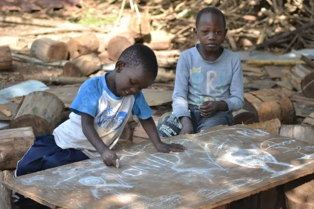 Zwei Kinder zeichenen etwas mit Kreide auf einen Stein